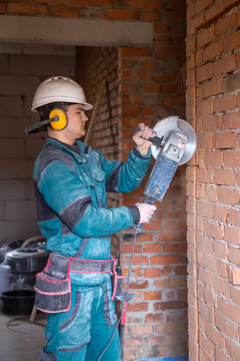 An electrician construction worker in a protective helmet at a work facility works with a grinder.